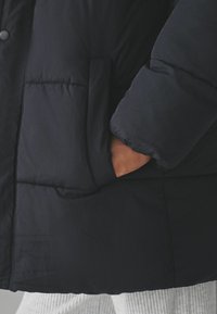 Marinblå pufferjakke med quiltet tekstur, der har en sidelomme og en blød overflade. Ærmet har en let gathered cuff-design.
