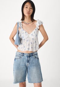 Květinový, lehký bílý crop top s volánkovými ramínky; spárován s mid-modrými džíny s odstřiženými lemy a standardními kapsami.