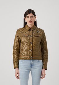 Giacca trapuntata verde oliva con colletto, due tasche sul petto e bottoni a pressione; presenta una texture liscia e lucida.