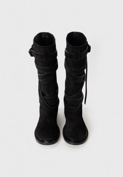 Para czarnych pielęgnacyjnym zamszowych, wysokich do kolan botków z wieloma okrążającymi paskami i klamrami, pokazana z przodu na białym tle.