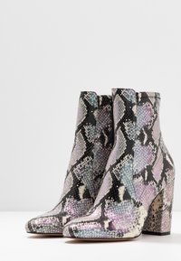 Ormskinnsankelstövlar med en glansig yta, flervidiga fjäll i lavendel, svart och vitt, med en blockklack för stabilitet.