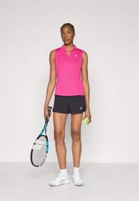 Różowy sportowy top bez rękawów, czarne spodenki, białe buty sportowe. Trzyma rakietę tenisową i żółtą piłkę tenisową. Gładka tkanina, sportowy design.