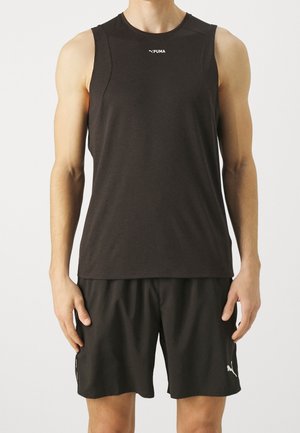 Mężczyzna w czarnej, bezrękawnikowej koszulce Puma i czarnych szortach Puma, stojący z ramionami swobodnie opuszczonymi wzdłuż ciała na białym tle.