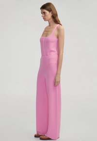 Roze gebreide jumpsuit met een aansluitende top, wijde pijpen, ronde halslijn en knoopdetails aan de voorkant. Glad textuur en lichtgewicht stof.