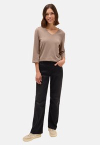 Beige V-neck pitkähihaine paita, yhdistettynä mustiin leveälahkeisiin housuihin ja beigeihin lenkkareihin. Pehmeä kangas, rento leikkaus, minimalistinen muotoilu.