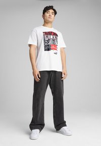 Camiseta blanca de algodón con un estampado gráfico en tonos rojos y negros. Combinada con pantalones vaqueros negros de corte holgado y zapatillas blancas.