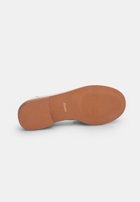 Talpă de încălțăminte de culoare deschisă, cu o textură netedă, având un model de striație din cauciuc și un branding auriu. Proiectată cu un vârf rotunjit și un toc mic.