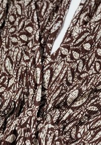 Tissu à motif marron et crème présentant un design de feuilles avec une texture striée, drapé et rassemblé pour ajouter de la texture et de la profondeur.