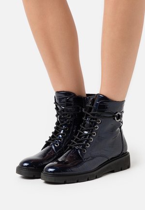 Bottines en cuir verni bleu marine avec une texture crocodile, bout rond, fermeture à lacets à l'avant et semelle noire robuste. Détails réglables sur le côté.