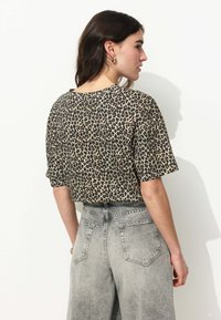 Haut à manches courtes en imprimé léopard couleur beige et noir, associé à un jean large taille haute gris clair avec poches arrière et quincaillerie minimaliste.