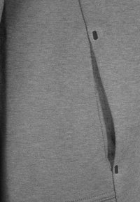 Grå sweatshirttyg med en slät textur; har en sidoficka med en diskret öppning. Enkelt, praktiskt design utan mönster eller accenter.