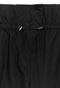 Pantalon à taille élastique noire avec cordons de serrage réglables maintenus par des stoppeurs argentés de chaque côté.