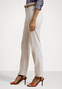 Off-white straight-leg jeans with subtle texture and side pockets, paired with brown strappy heels featuring an ankle strap and orange accents.