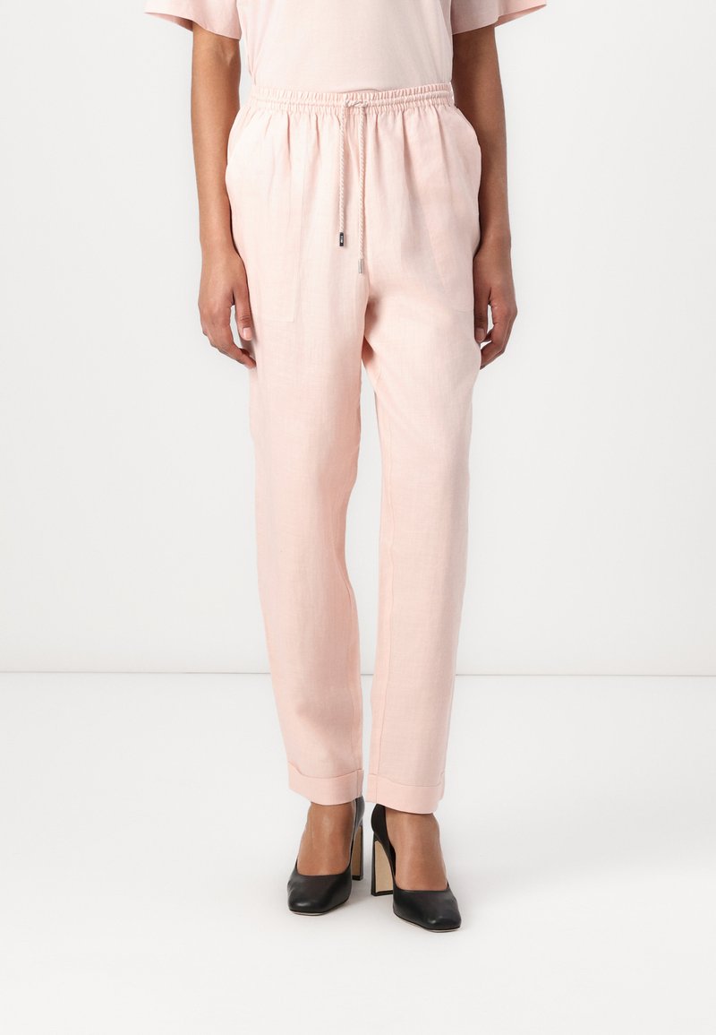 Light pink linen trousers with an elastic waistband, drawstring closure, two side pockets, and tapered legs, paired with black high heels.