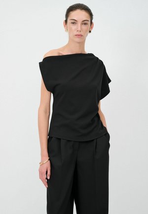 Top nero scoperto sulle spalle in tessuto liscio con design drappeggiato. Abbinato a pantaloni neri a vita alta. Stile minimalista, senza pattern né grafiche.