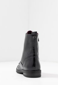 Bottine en cuir noir avec une finition lisse, des détails brogue subtils, un bout rond et un petit talon, dotée d'une languette à l'arrière et d'accents de couture.