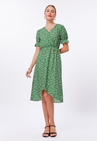 Grünes Blumenmusterkleid mit V-Ausschnitt, kurzen Puffärmeln und Wickeldesign. Es hat einen asymmetrischen Saum und drei dekorative Knöpfe in der Taille.