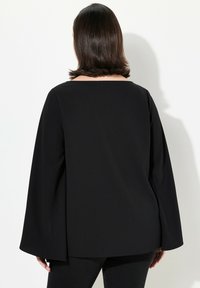 Top nero con scollatura quadrata e maniche lunghe e larghe. Realizzato in tessuto morbido, presenta un design semplice e privo di decorazioni.