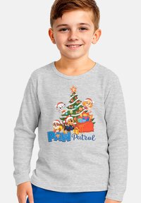 Una maglietta grigio a maniche lunghe presenta una grafica colorata di "Paw Patrol" con un albero di Natale e personaggi canini animati che indossano cappelli di Babbo Natale.