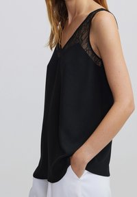 Black sleeveless top with lace accents at the shoulders, featuring a loose fit and soft texture. The design has a V-neckline.