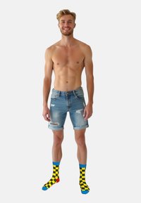 Lysblå denim shorts med slidte detaljer, parret med multifarvede sokker med et gult og sorte ternet mønster.