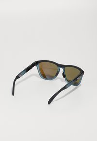 Ochelari de soare cu ramă mată neagră, accente albastre și lentile polarizate de culoare maro. Prezintă un design sportiv și brate texturate pentru aderență.