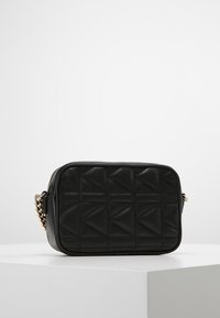 Borsa a tracolla in pelle nera con motivo trapuntato a triangoli, chiusura con cerniera e tracolla a catena dorata. Forma rettangolare, texture liscia.