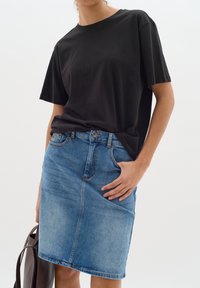 Svart bomullströja i kombination med en ljusblå denimkjol med rak skärning och framfickor. Modellen håller en mörkbrun väska.