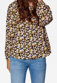 Blusa a stampa floreale con sfondo nero e petali gialli, viola e bianchi, maniche lunghe e vestibilità ampia.