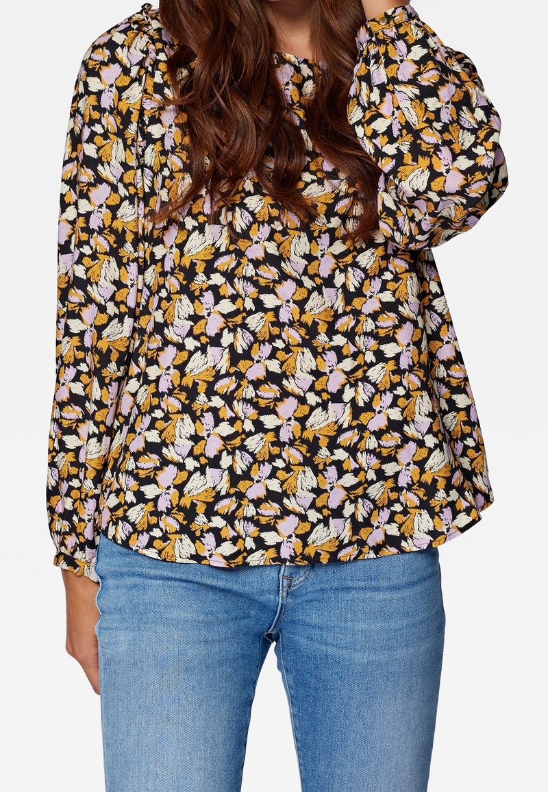 Blusa a stampa floreale con sfondo nero e petali gialli, viola e bianchi, maniche lunghe e vestibilità ampia.