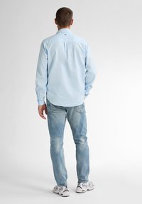 Světle modrá košile s dlouhým rukávem a límečkem na knoflíky, v kombinaci s vybledlými modrými džíny a bílými teniskami. Košile má zadní sklady.