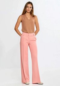 Brązowy top bez rękawów z dekoltem w serek oraz różowe spodnie o szerokich nogawkach z dwoma guzikami. Gładka tkanina o miękkiej fakturze.