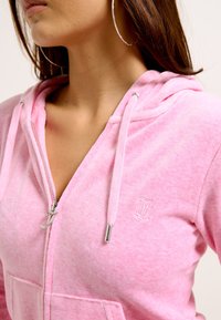 Felpa con zip rosa caratterizzata da una texture morbida, tasche frontali e logo ricamato, con zip e accessori del cappuccio color argento.