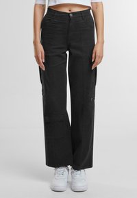 Pantaloni cargo neri con vestibilità rilassata, tasche con zip e chiusura a pulsante. Il materiale sembra resistente con una texture liscia.