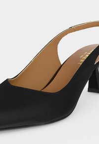 Μαύρο παπούτσι slingback με χαμηλό τακούνι τύπου block και ταμπά εσωτερική επένδυση, που δείχνει πλευρική και μερική επάνω όψη σε λευκό φόντο.