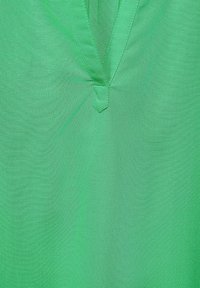 Grön v-ringad skjorta med ett slätt, lättviktsmaterial. Har en mittsöm detalj vid halsringningen och en enhetlig färg utan mönster.