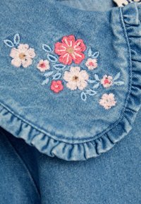 Tessuto di denim con colletto arricciato, caratterizzato da un ricamo floreale colorato in rosa, bianco e blu, che mette in mostra dettagli e texture intricate.