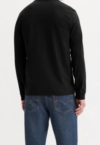 Camiseta negra de manga larga con un escote redondeado, combinada con jeans de mezclilla azules que tienen costuras en contraste y dos bolsillos traseros.