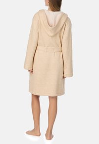 Beżowy szlafrok z kapturem wykonany z miękkiego, teksturowanego materiału, z paskiem w talii i długimi rękawami, z przytulnym, futerkowym wnętrzem.