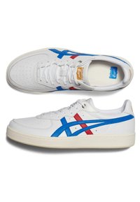 Białe sneakersy z niebieskimi i czerwonymi akcentami, gładka skóra, perforowany nosek, płaskie sznurówki oraz teksturowana podeszwa. Logo na języku.