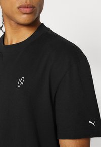 Czarny bawełniany t-shirt z okrągłym dekoltem, krótkimi rękawami oraz białym haftowanym logo na piersi i rękawie. Gładka tekstura.