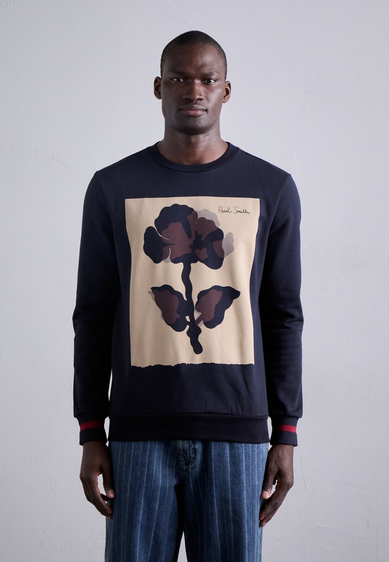 Marineblaues Sweatshirt mit großem abstraktem Blumenmuster in dunklen Brauntönen auf einem beigen Hintergrund. Rote Akzente an den Bündchen. Klassisches Rundhalsdesign.