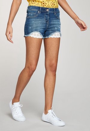 Shorts en denim avec un délavage bleu, ourlet en dentelle blanche festonnée, design à cinq poches et fermeture à bouton. Associés à des baskets en toile blanches.
