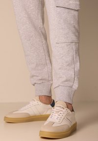 Pantaloni della tuta grigi con tasche laterali, abbinati a sneakers bianche e beige con suola in gomma e dettagli di cucitura discreti.