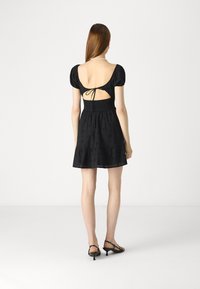 Μαύρο κοντό φόρεμα με φουσκωτά μανίκια και ανοιχτή πλάτη, διαθέτοντας σμιλευμένο μπούστο και φούστα με κλος σχέδιο με λουλούδια. Μαύρες σανδάλια με λουράκια.