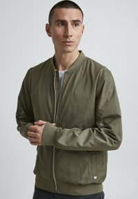 Olivegrüne Bomberjacke aus glattem, leichtem Material. Mit gerippten Bündchen und Kragen, Frontreißverschluss und Seitentaschen.