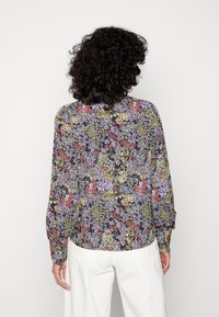 Blusa de mangas longas com um padrão floral escuro em tons de roxo, vermelho e verde, feita de um tecido leve com um corte descontraído e bainha arredondada.