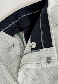Grå ternet stof med et elegant design, der har en marineblå inderside, knapdetalje og kontrasterende grøn syning langs kanterne.