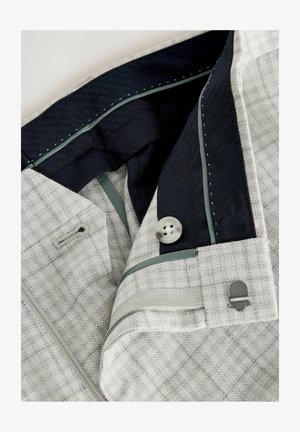 Grau kariertes Gewebe mit einem eleganten Design, das ein navyblaues Innenfutter, eine Knopfdetail und kontrastierendes grünes Stichen entlang der Kanten aufweist.