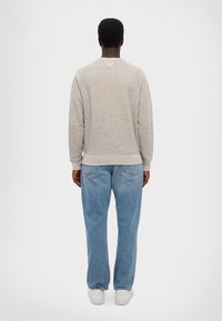 Grey textured sweatshirt with a rounded neckline, paired with light blue jeans and white sneakers, shown from the back.